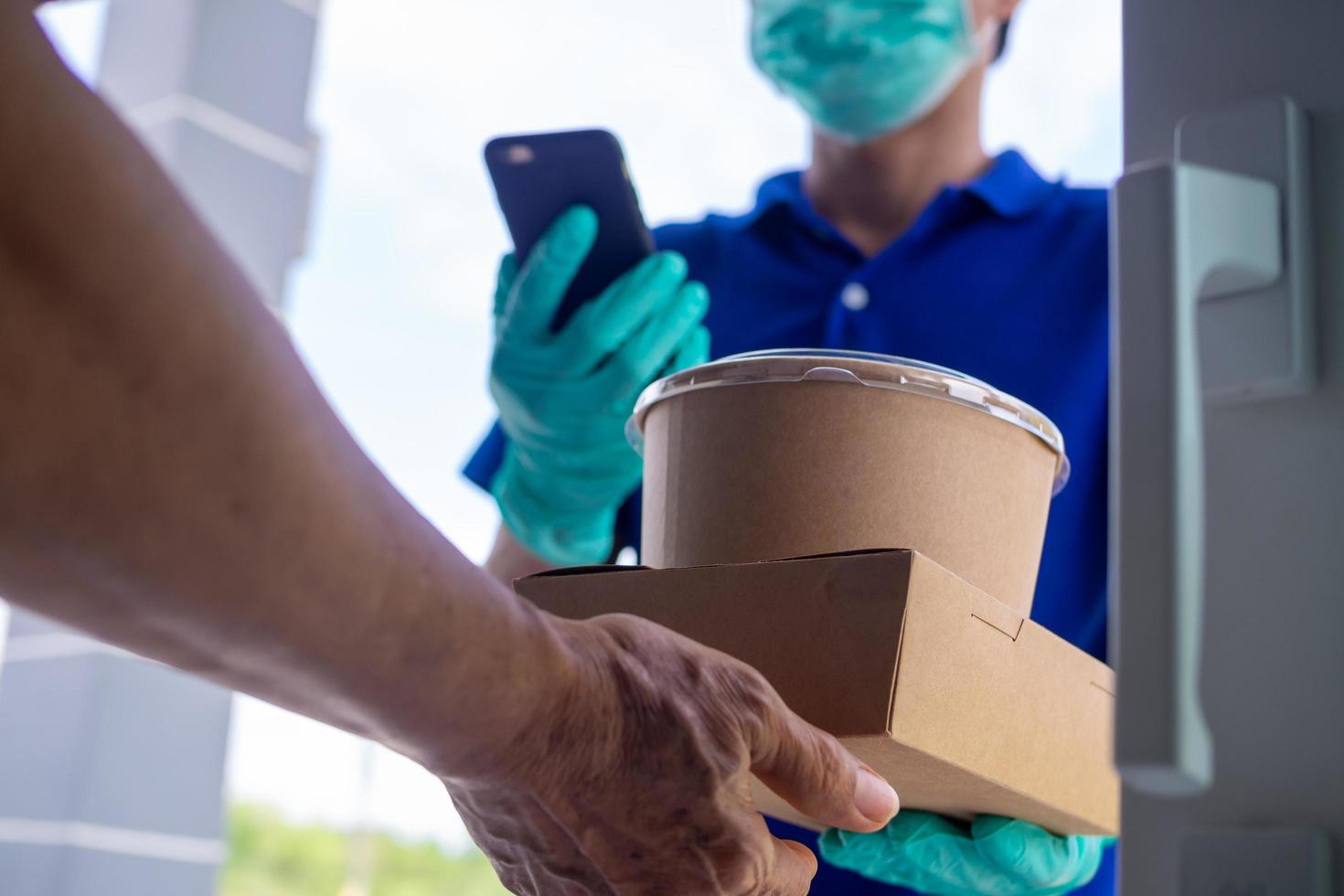 les commandes en ligne acceptent les boîtes de nourriture du livreur portant un uniforme bleu avec des masques et des gants. prendre le petit déjeuner à la maison. l'expéditeur dispose d'un service pour livrer rapidement des produits ou de la nourriture photo