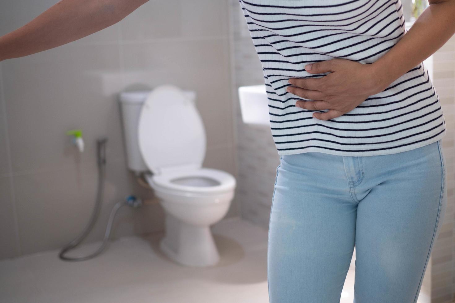 les femmes se tiennent devant la porte de la salle de bain en utilisant leurs mains pour tenir l'abdomen avec de fortes douleurs abdominales ou de la diarrhée. le concept de crampes d'estomac, diarrhée photo