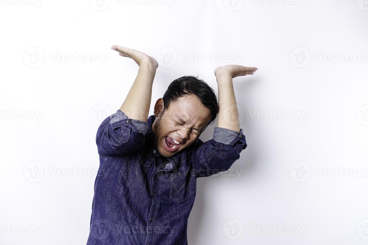 homme asiatique choqué portant une chemise bleue pointant vers l'espace de copie au-dessus de lui, isolé sur fond blanc photo