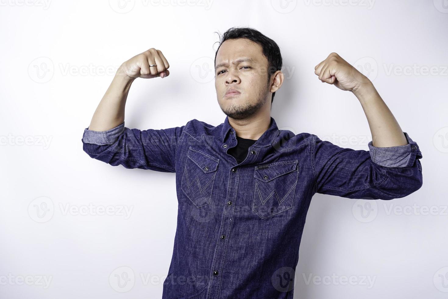 homme asiatique excité portant une chemise bleue montrant un geste fort en levant les bras et les muscles en souriant fièrement photo