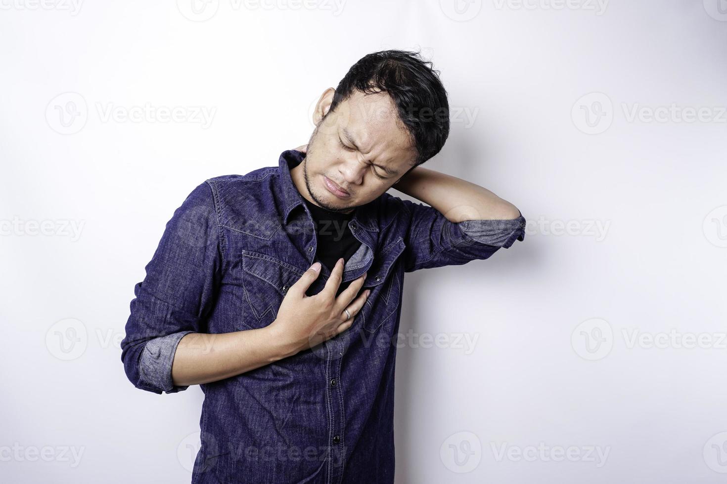 un jeune homme fatigué et bouleversé porte une chemise bleue souffrant de douleur, de spasmes musculaires sur le lieu de travail. fatigue, délai, douleur et posture incorrecte photo