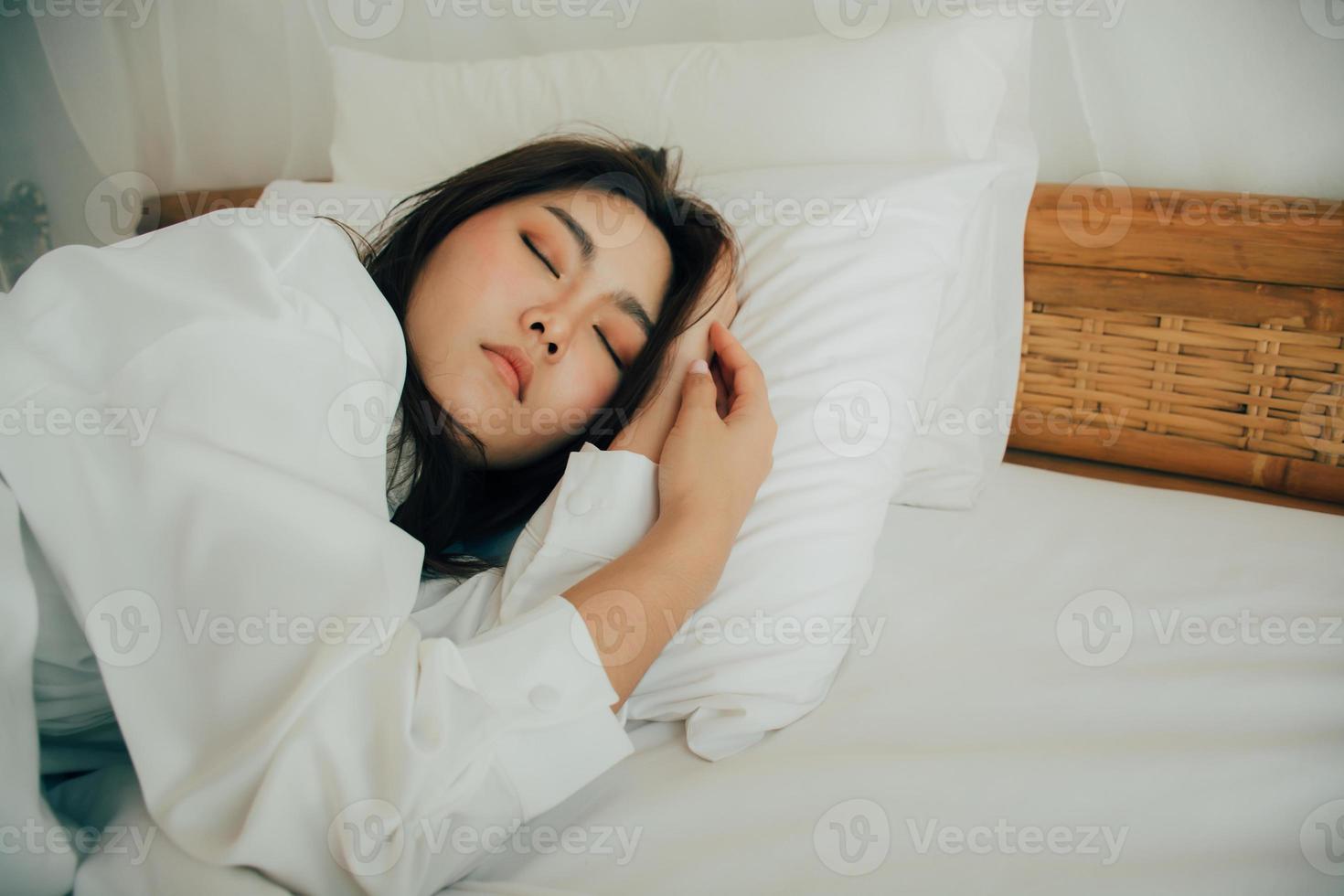 jeune femme dormant dans son lit, sa tête reposant sur un oreiller blanc avec ses mains à côté de sa tête. belle fille aime le linge de lit frais et doux et le matelas dans la chambre. concept de bonne nuit de sommeil. photo