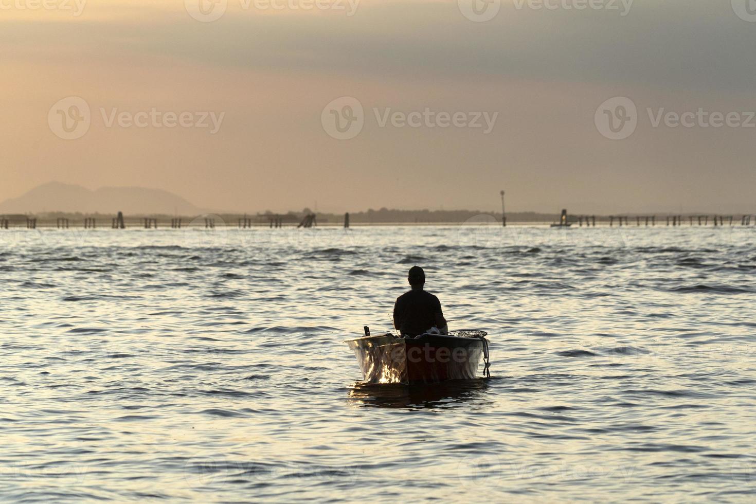 silhouette de pêcheur au coucher du soleil dans le port de chioggia lagune de venise depuis un bateau photo