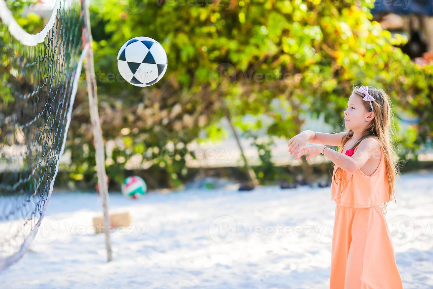 petite fille active jouant au volley-ball sur la plage avec ballon. flid sportif appréciant le jeu de plage à l'extérieur photo