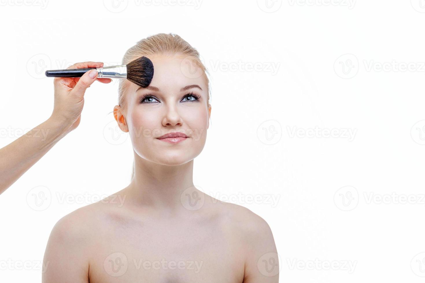 main de maître de maquillage appliquant de la poudre pour le modèle de jeune femme sur fond blanc. maquillage professionnel appliqué par l'artiste. beau visage de fille avec une peau parfaite. détail de maquillage en cours. photo