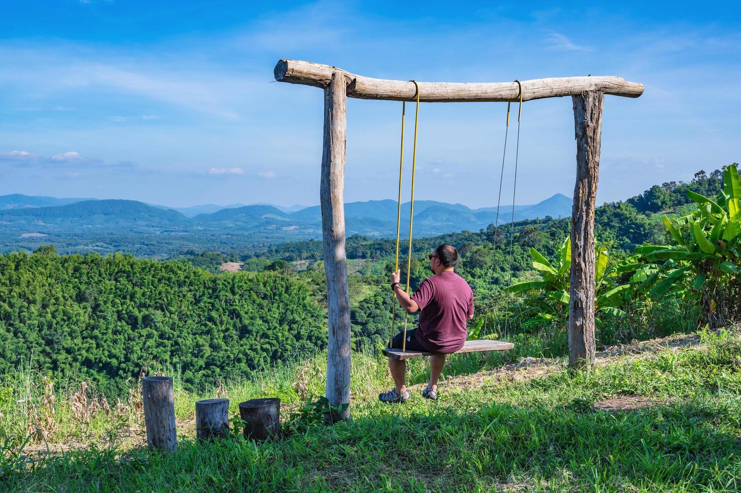 gros gars asiatique assis sur une balançoire en bois avec une belle vue sur le paysage de phu lamduan à loei thailand.phu lamduan est une nouvelle attraction touristique et un point de vue sur le fleuve mékong entre la thaïlande et les loas. photo