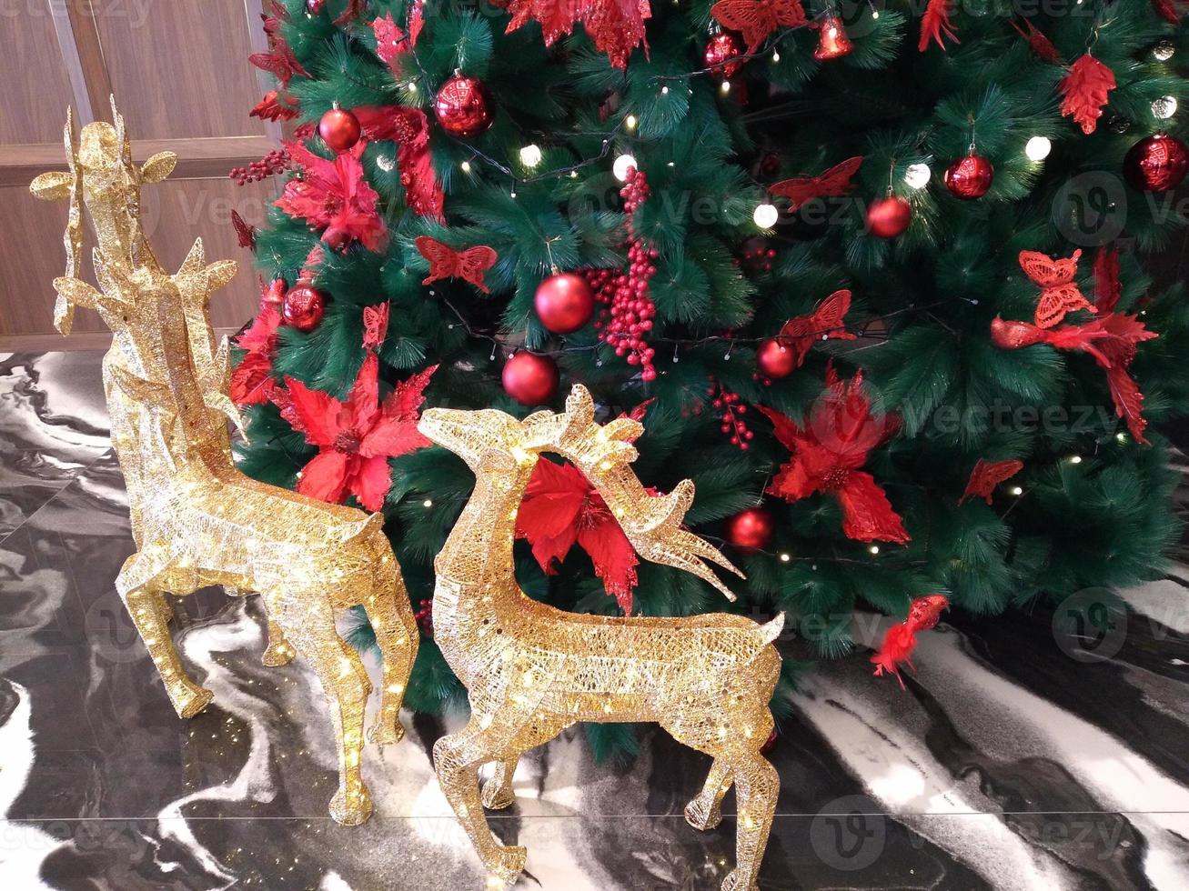 le sapin de noël est décoré d'arcs rouges et d'arcs rouges et est entouré de rennes dorés étincelants photo