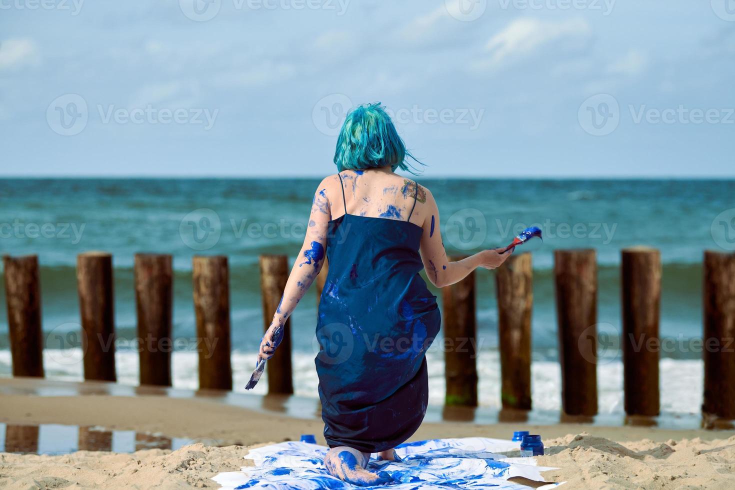 artiste de performance artistique femme aux cheveux bleus enduite de peintures à la gouache bleue dansant sur la plage photo