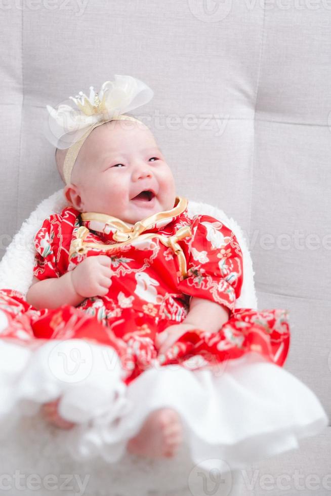 gros plan mignon bébé nouveau-né en body rouge allongé seul sur le lit. adorable bébé repose sur des draps blancs, regardant la caméra à l'air paisible. petite enfance, soins de santé et pédiatrie, concept de petite enfance. photo