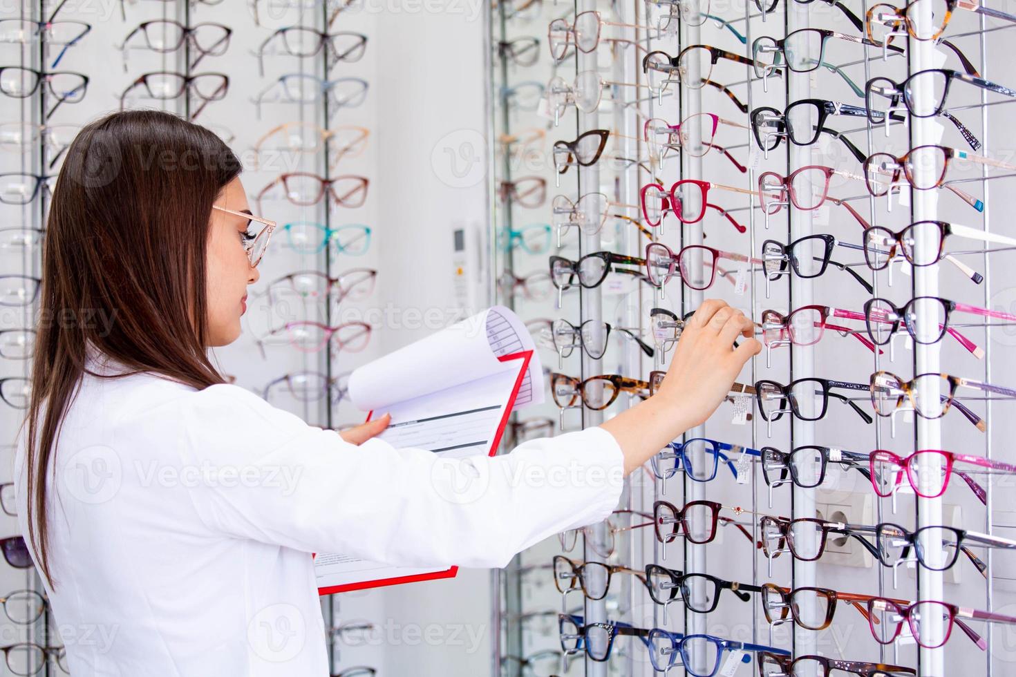 jolie ophtalmologiste écrivant des données dans un presse-papiers, travaillant dans un magasin d'optique. concept de soins de santé et de médecine photo