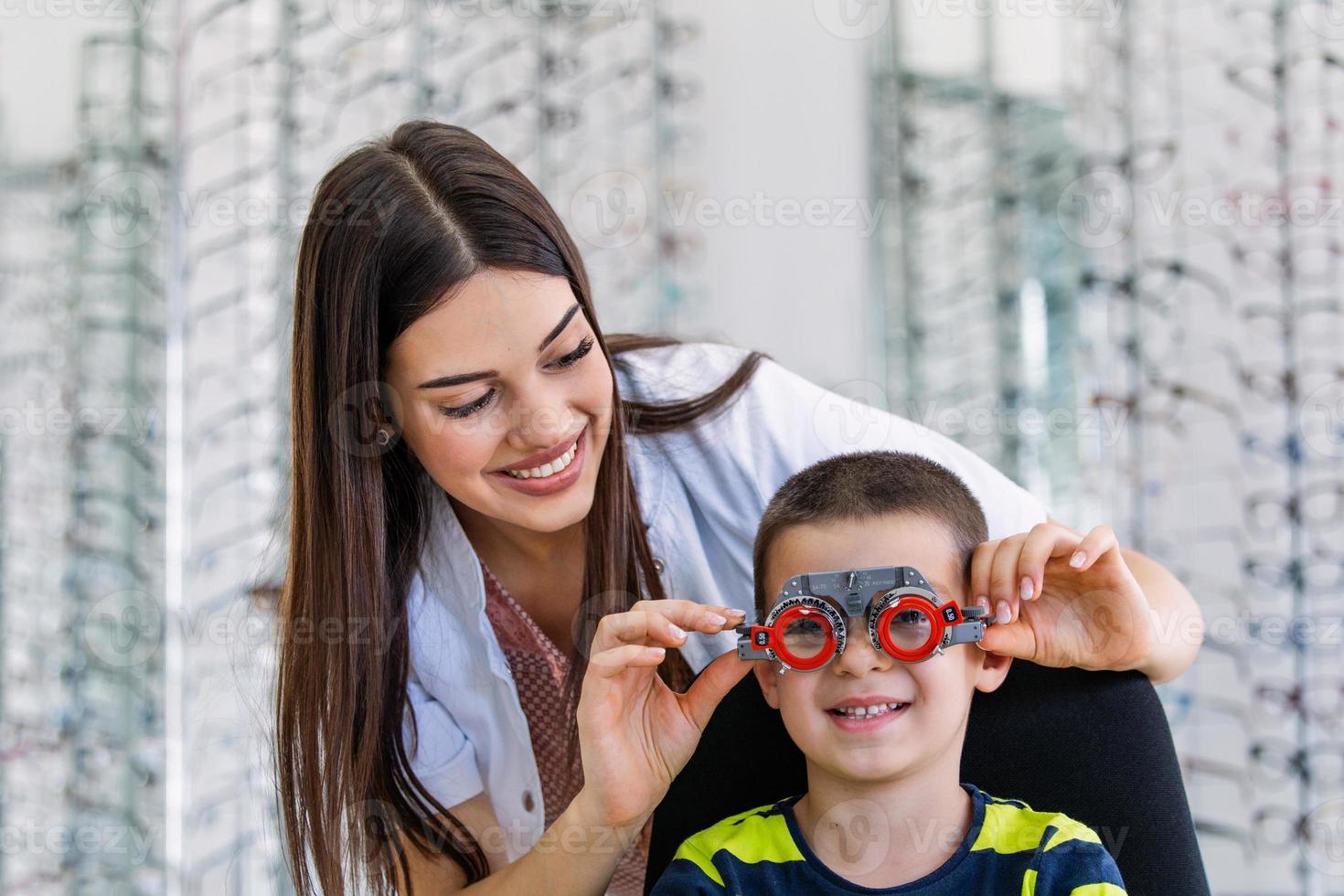 un jeune garçon souriant est assis et regarde la caméra pendant le contrôle de la vision. l'ophtalmologiste utilise un équipement médical spécial pour sauver et améliorer la santé des yeux. photo