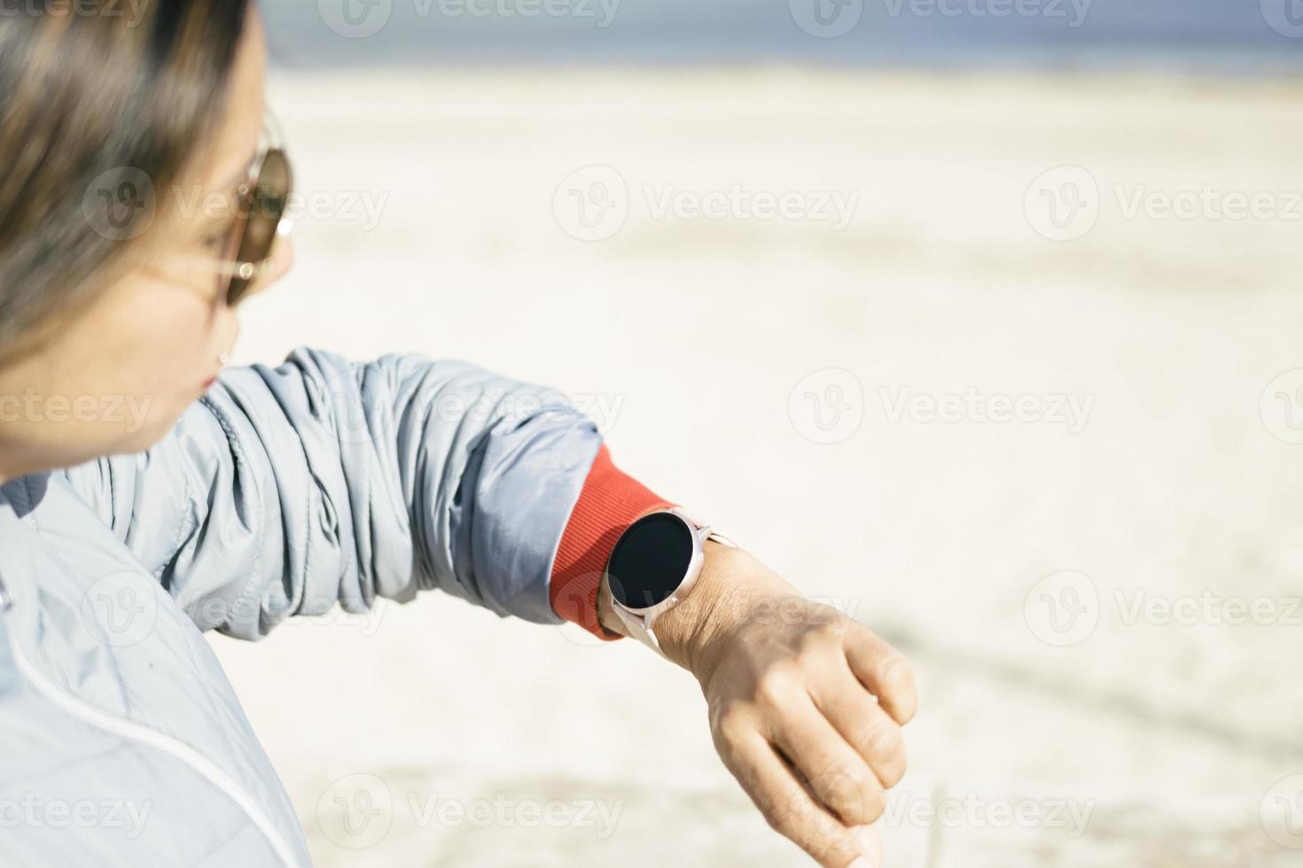 vue latérale fermée, femme latina avec des lunettes de soleil regardant une montre intelligente, fond clair photo