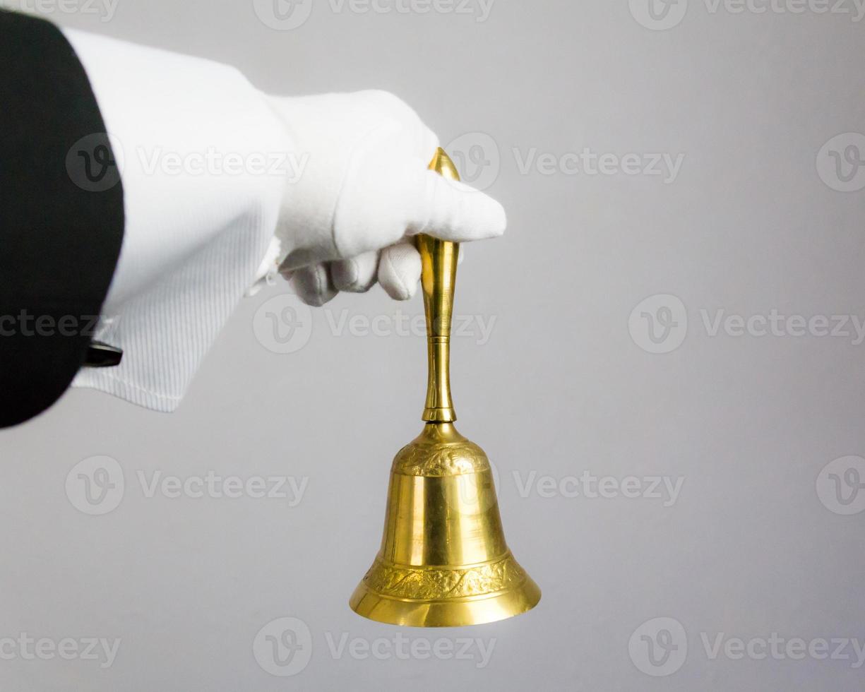 image isolée d'une main gantée blanche tenant une cloche d'or sur fond blanc. anneau pour le concept de service. hospitalité professionnelle et élégance. photo