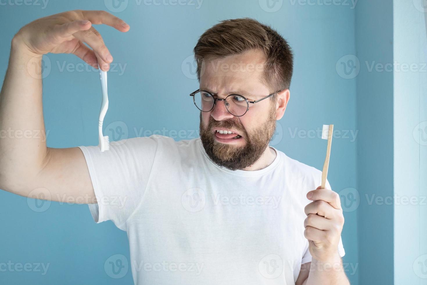 l'homme opte pour une brosse à dents en bambou biodégradable et méprise la brosse en plastique. concept éco. photo