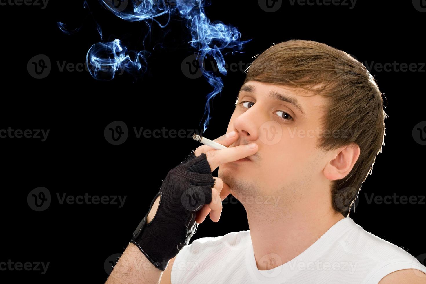 jeune homme fumant une cigarette. isolé sur noir photo