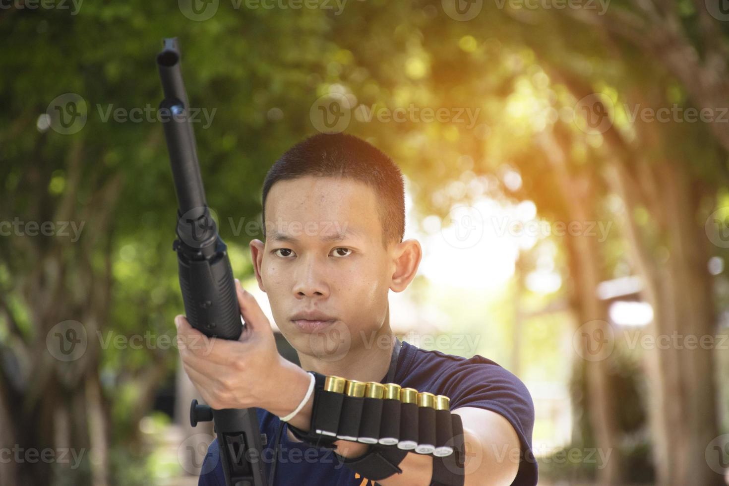 portrait d'un tireur de fusil de chasse asiatique tenant un fusil de chasse à la main sous l'arbre, lumière du soleil éditée, concept d'activité récréative dans le monde entier. photo