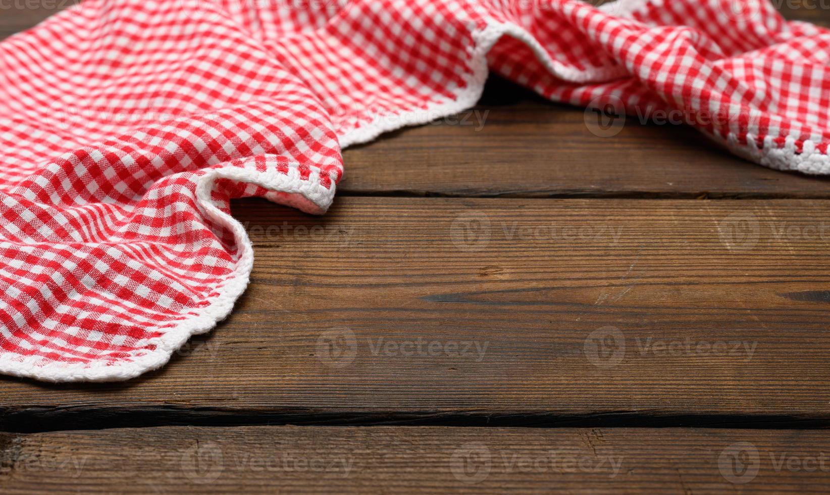 serviette de cuisine en coton rouge et blanc pliée sur fond marron en bois, vue de dessus photo