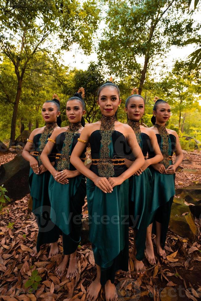 des femmes asiatiques glamour avec des costumes verts et du maquillage s'alignent dans la jungle avec des feuilles brunes sur le sol photo