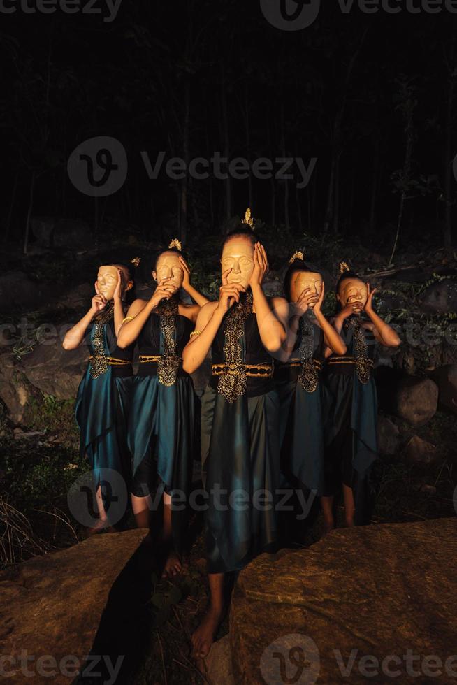 un groupe de femmes asiatiques portant des masques en bois en costumes verts tout en se tenant entre les rochers à l'intérieur de la forêt photo