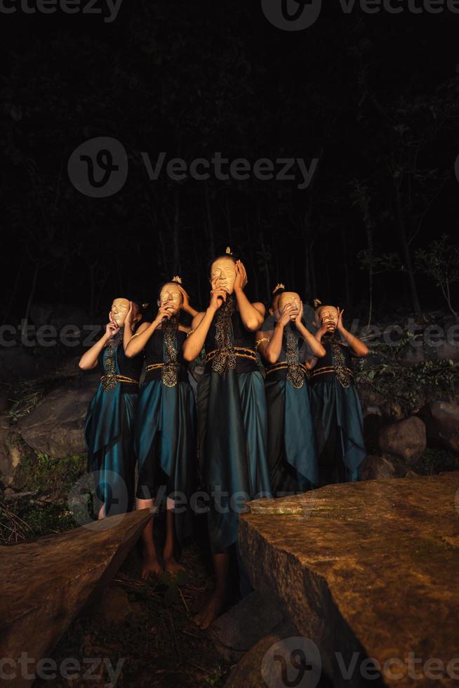 un groupe de femmes indonésiennes tenant et portant un masque en bois marron dans une jupe verte entre le rocher photo