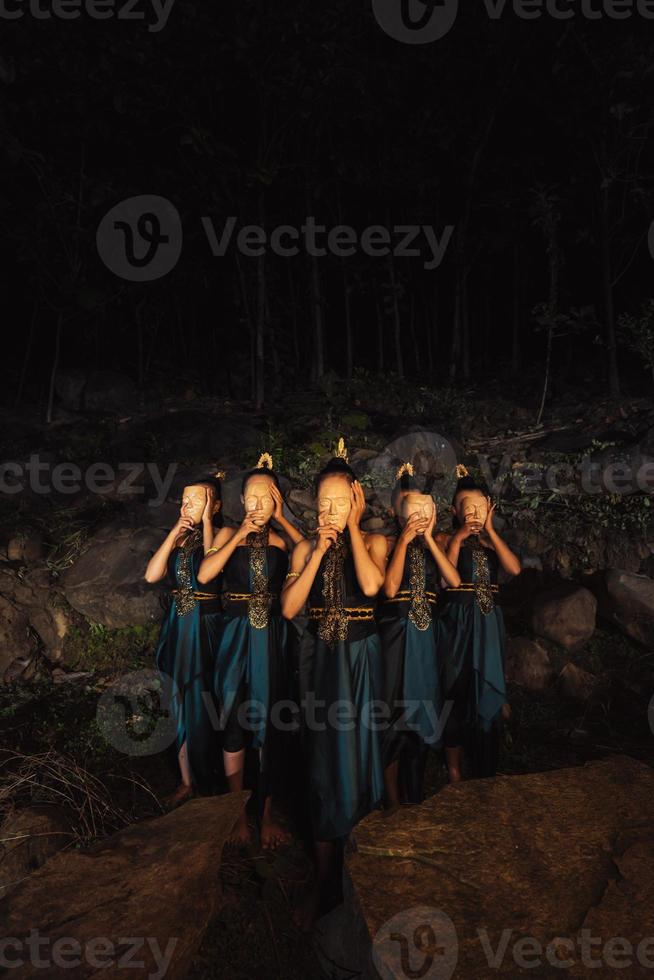 un groupe de femmes indonésiennes tenant et portant un masque en bois marron dans une jupe verte entre le rocher photo