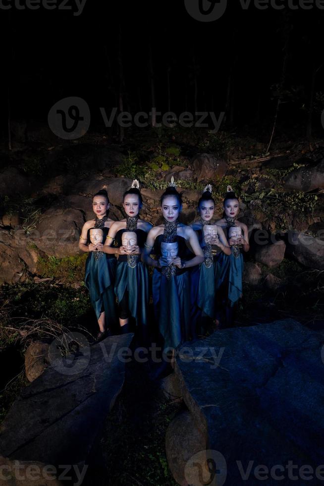un groupe de femmes javanaises debout dans les bois entre les rochers tout en tenant un masque en bois photo