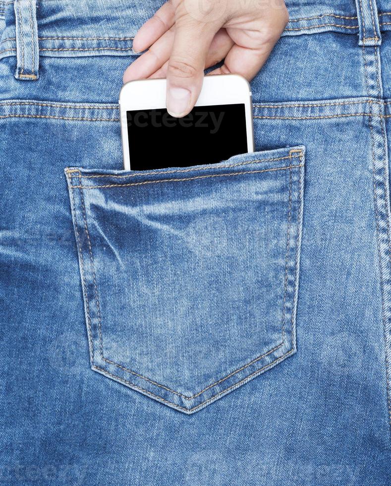 la main féminine tient un téléphone blanc à l'arrière du jean bleu photo