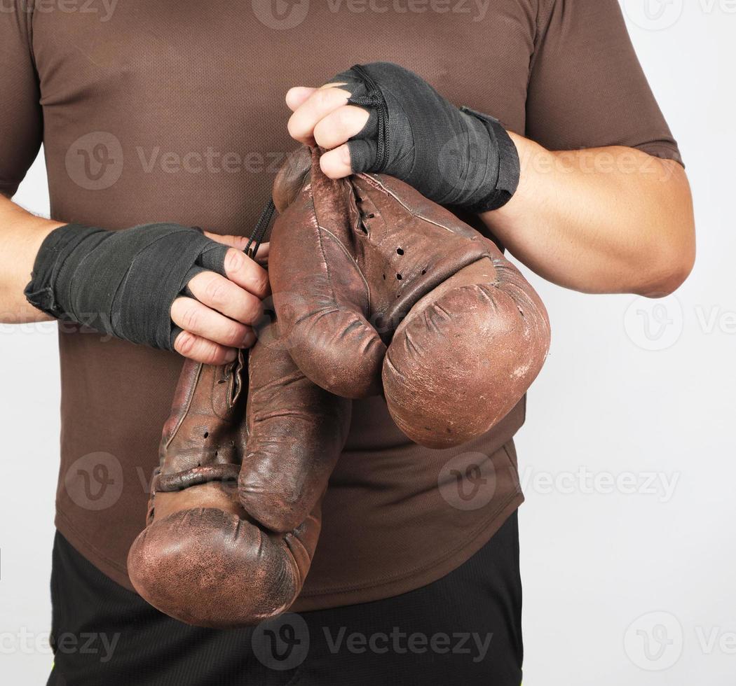 homme adulte en uniforme de sport brun tient une paire de gants de boxe décontractés vintage bruns photo