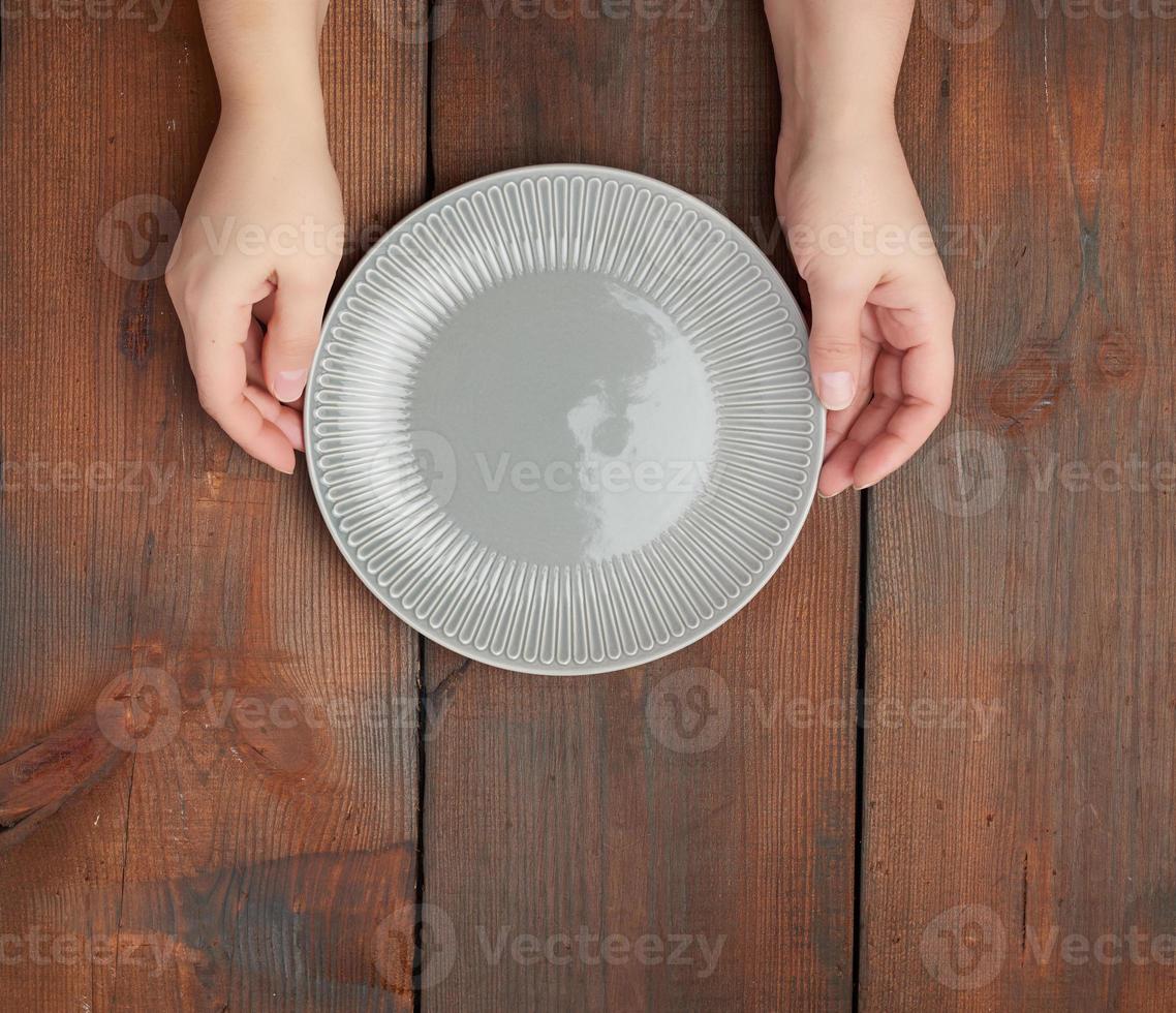 les mains tiennent une assiette en céramique ronde grise vide, fond en bois photo