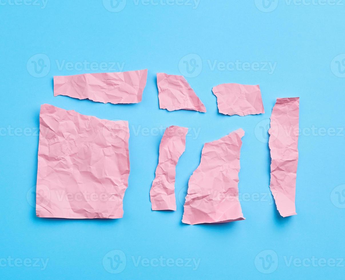 ensemble de divers morceaux coupés de papier froissé rose sur fond bleu photo