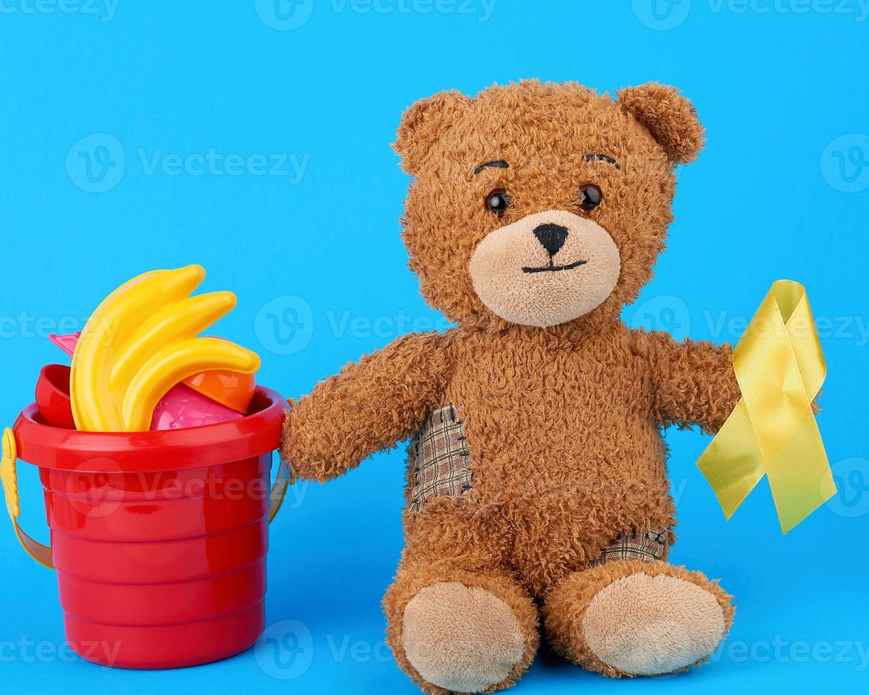 ours en peluche brun est assis et tient dans sa patte un ruban de soie jaune photo