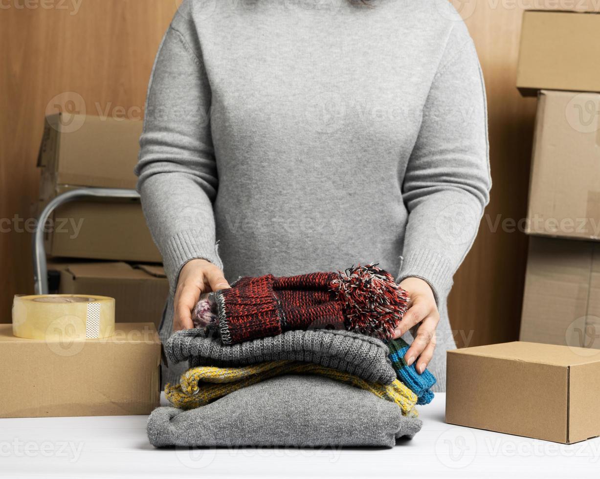 femme en pull gris ramasse des vêtements dans une boîte, concept d'assistance et de bénévolat, déménagement photo