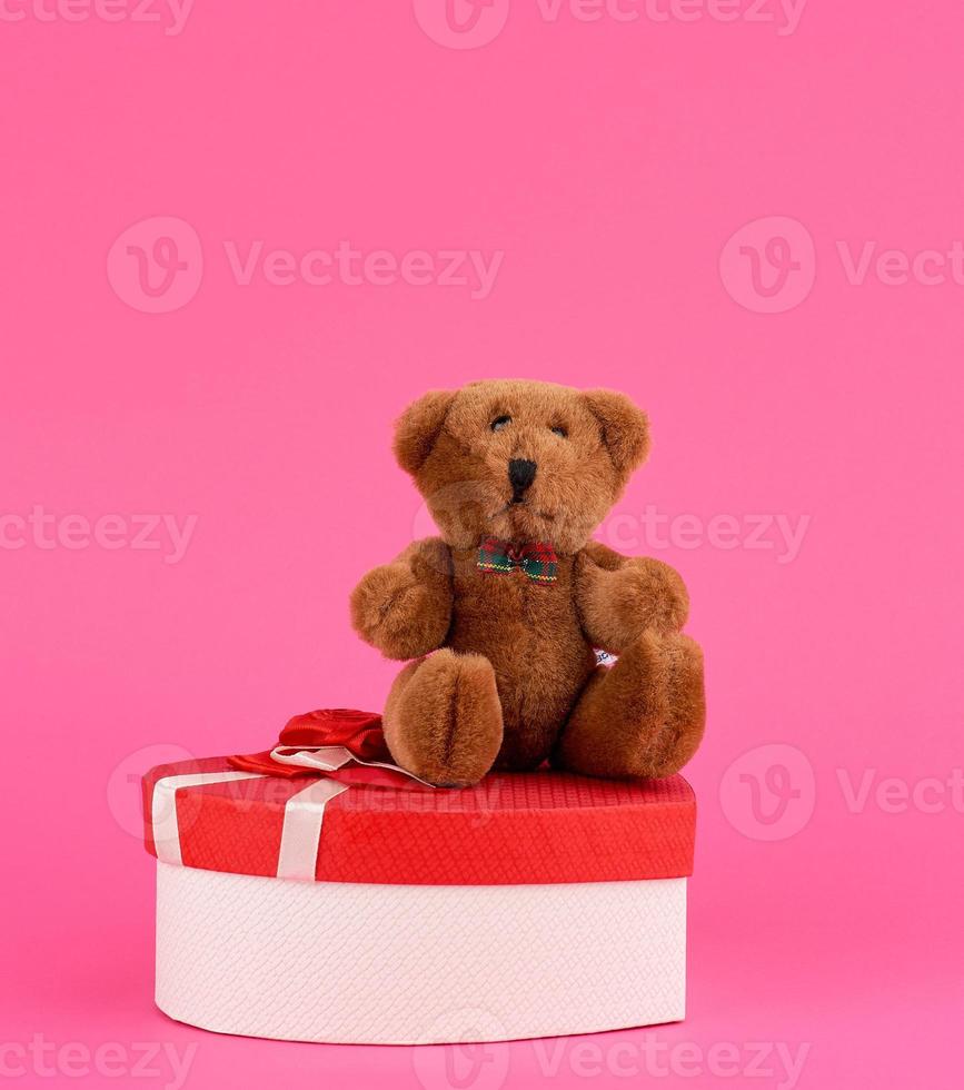 mignon ours en peluche marron et boîte cadeau rouge sur fond rose photo