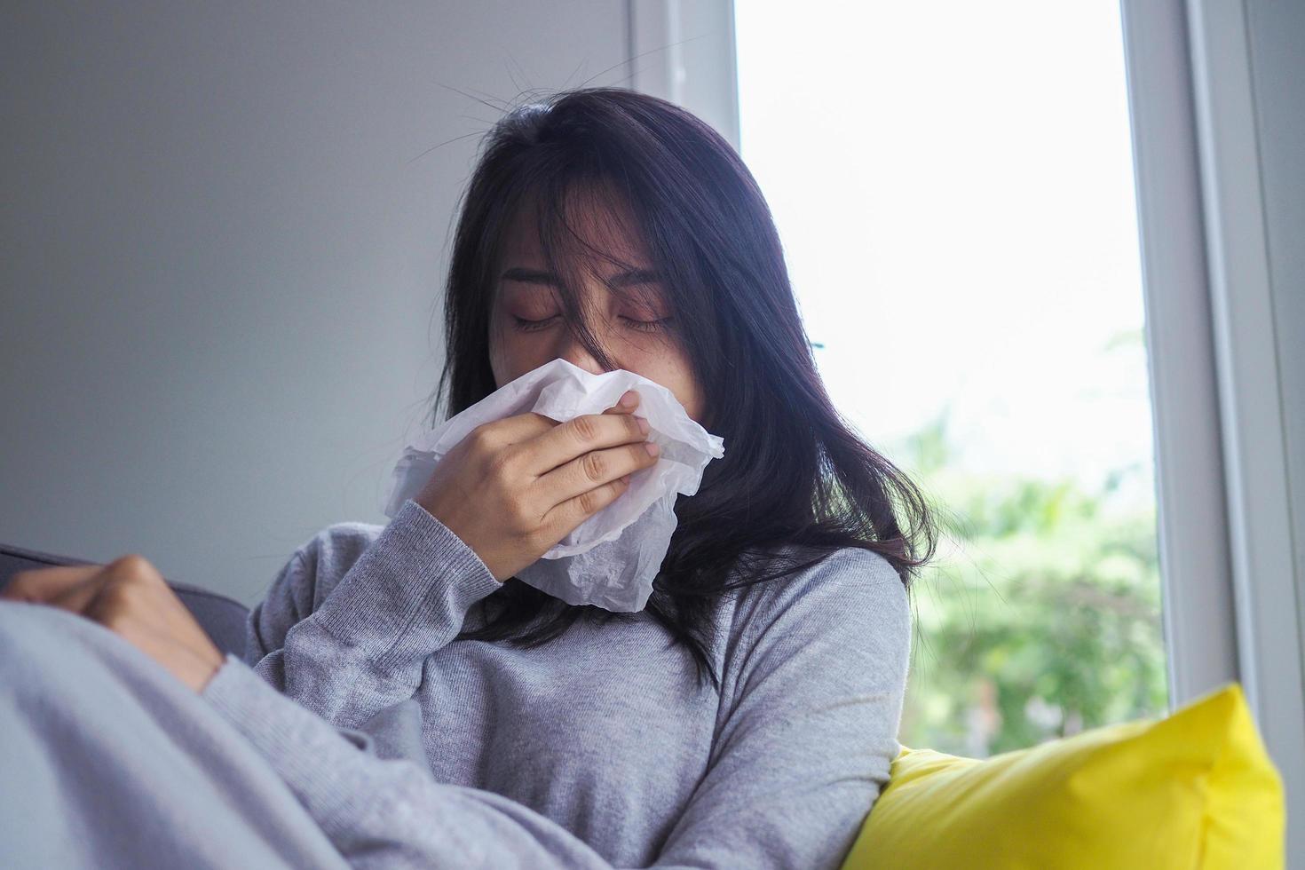 fille malade assise sur le canapé de la maison, ayant une fièvre nasale qui coule et s'essuyant avec un mouchoir malade. concept de froid et d'éternuement photo