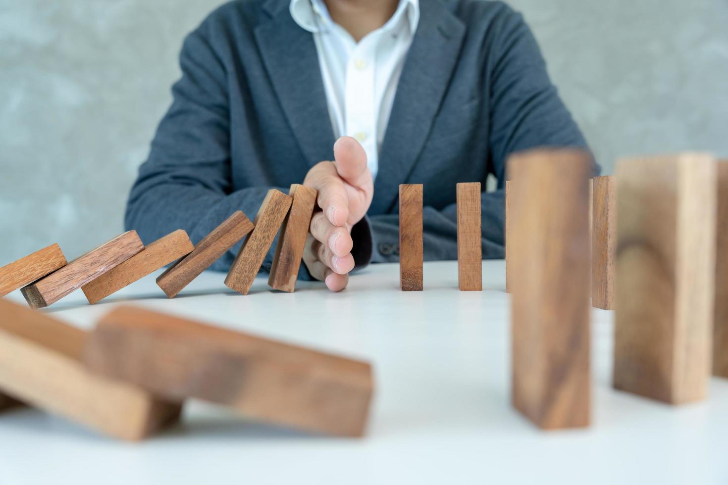 l'assurance avec les mains protège le domino. les mains de l'homme d'affaires empêchent les dominos de tomber dans la crise des affaires. contrôle des risques commerciaux et planification et stratégies pour gérer les entreprises d'assurance. photo