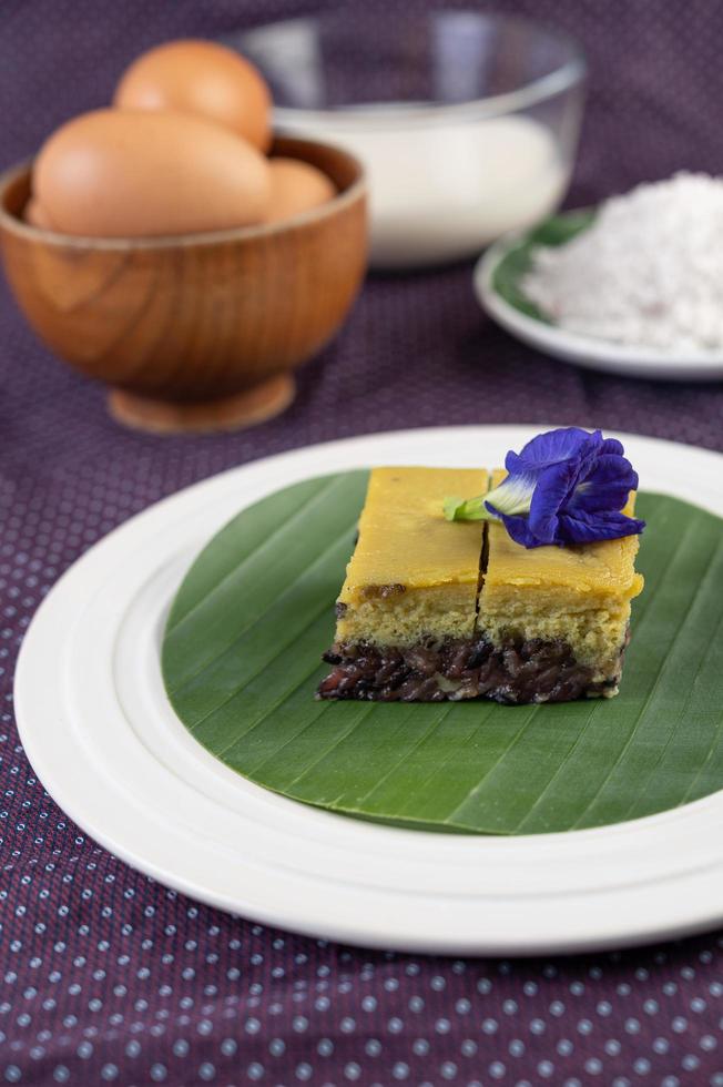 Riz gluant noir sur une feuille de bananier dans une assiette blanche avec des fleurs de pois papillon photo