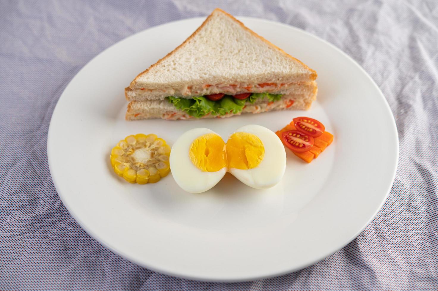 oeufs durs, maïs, sandwich aux tomates sur une plaque blanche photo