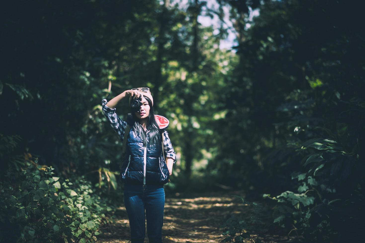 Jeune femme en sweat à capuche tenant un appareil photo rétro et prendre des photos dans la forêt