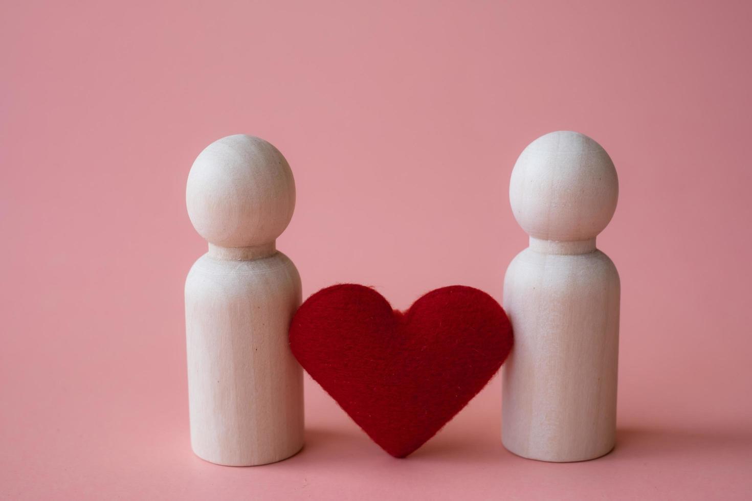 forme de coeur rouge entre figurines en bois de l'homme et de l'homme sur fond rose. aimer le concept lgbtq. concept de minorités et de communautés sexuelles photo