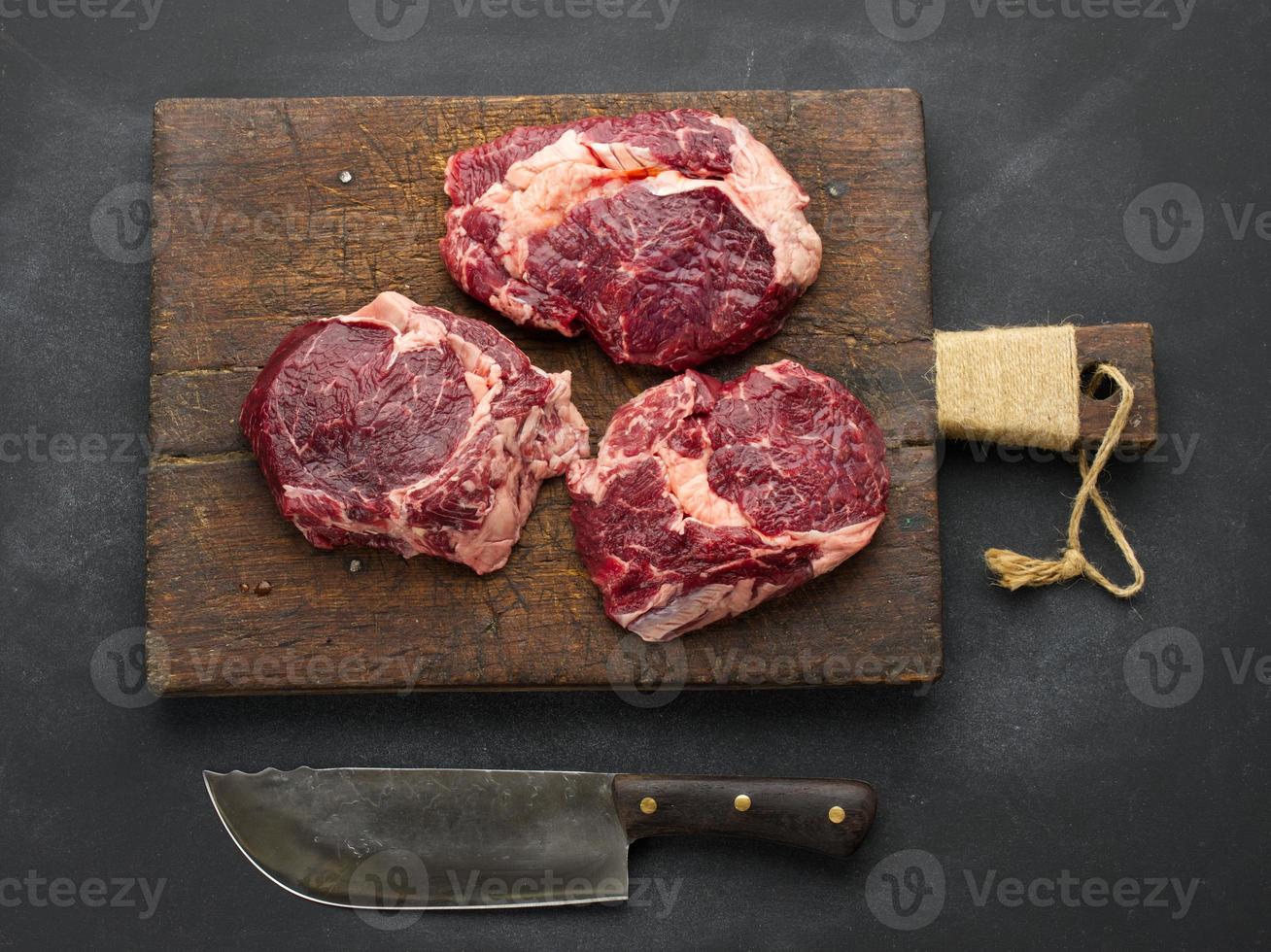 couteau et morceau cru de faux-filet de boeuf sur un tableau noir, vue de dessus photo