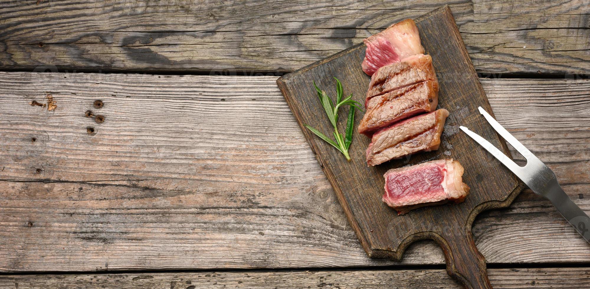 Steak de bœuf frit tranché contre-filet de New York sur une planche à découper en bois, degré de cuisson rare, vue de dessus photo