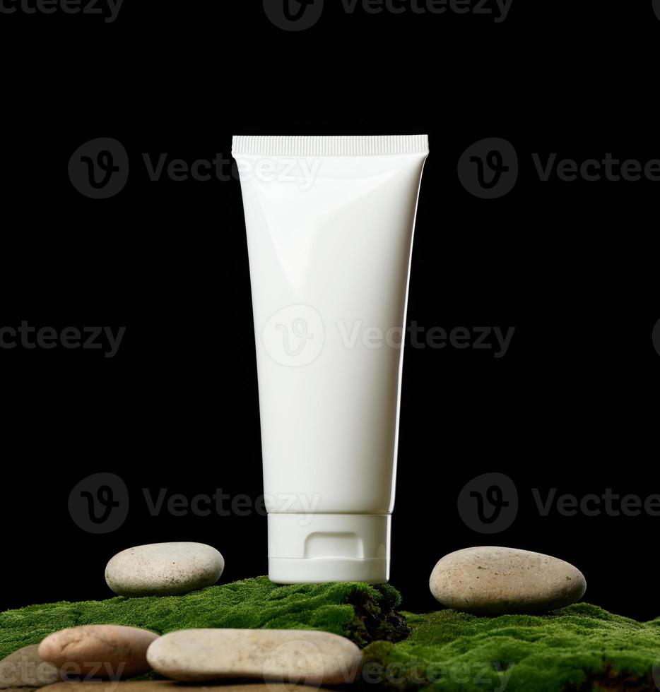 tubes en plastique blanc vides pour cosmétiques se dressent sur mousse verte, fond noir. emballage pour crème, gel, sérum, publicité et promotion de produits, maquette photo