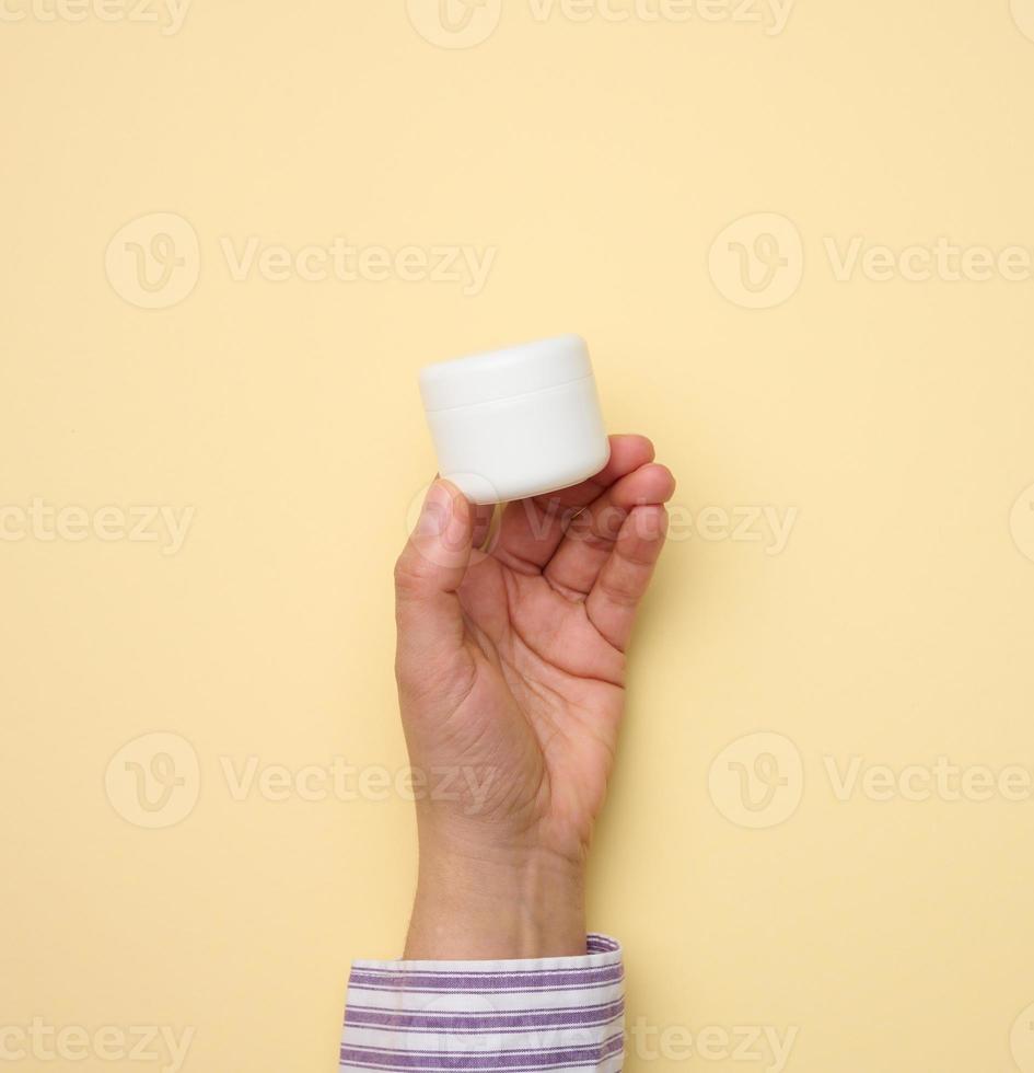 main féminine tenant un pot en plastique blanc. emballage pour crème, gel, sérum, publicité et promotion de produits photo