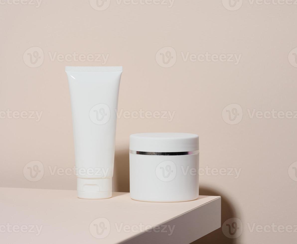 un tube en plastique blanc vide et un pot pour cosmétiques se dressent sur un fond beige. récipients pour crème, shampooings, substances liquides. image de marque, modèle photo