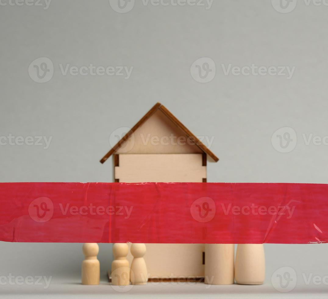 famille de personnages en bois et une maison en bois derrière un ruban rouge sur fond gris. concept de quarantaine, verrouillage pendant une pandémie et une épidémie. photo