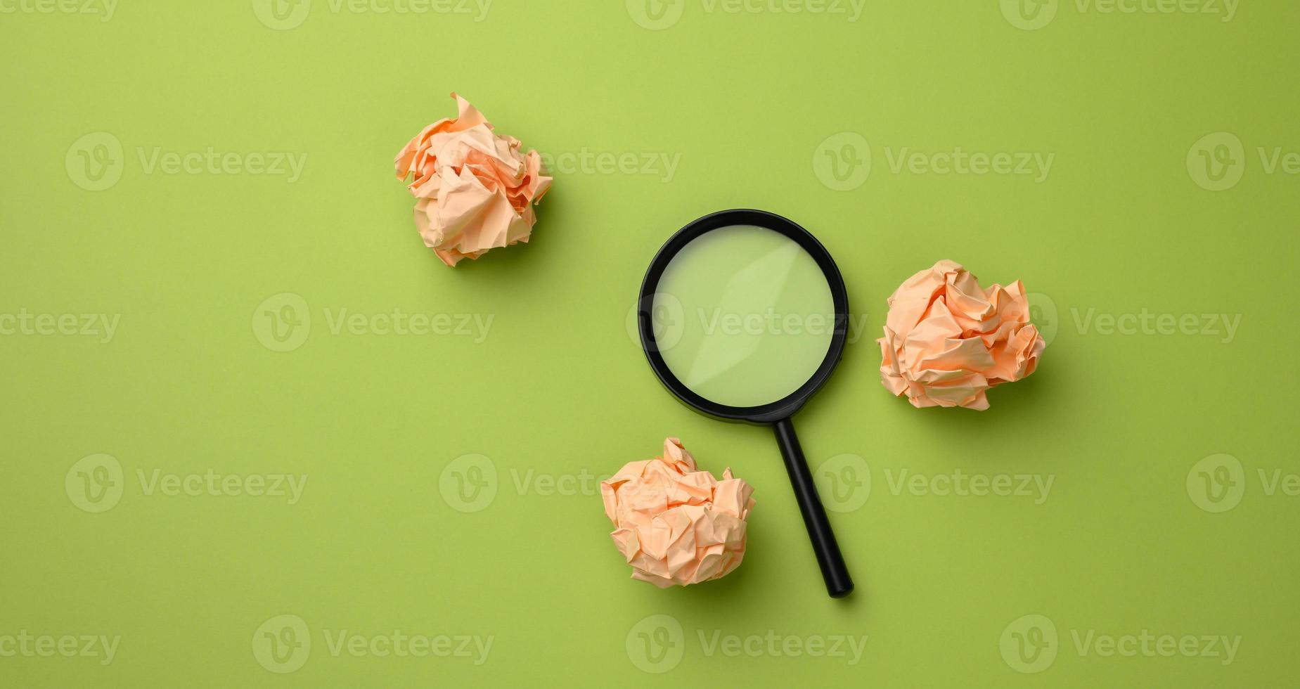 boules de papier froissées et loupe en plastique noir sur fond vert. concept de recherche d'idées photo