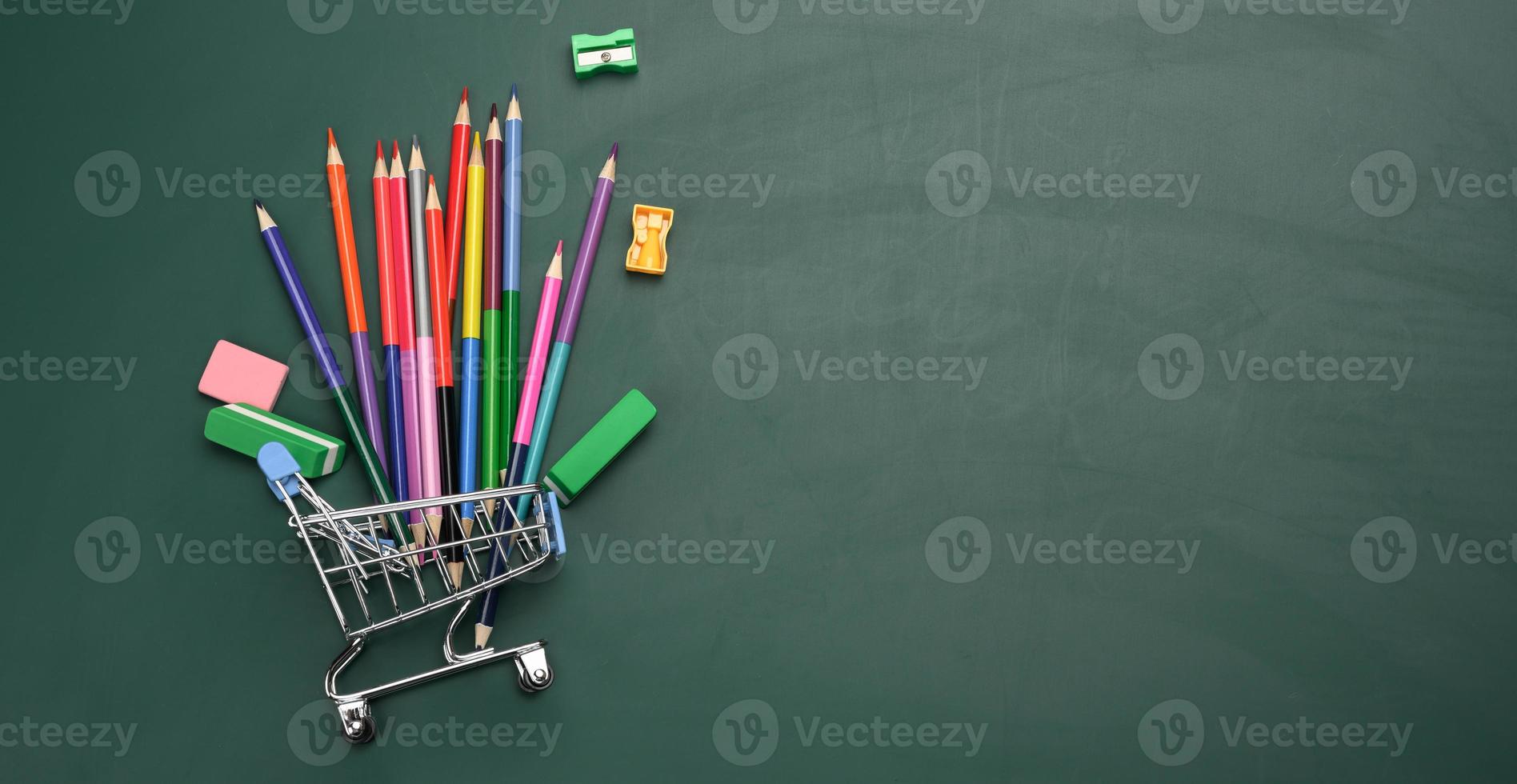 panier miniature rempli de fournitures de bureau scolaires sur un tableau de craie verte. préparer l'école, acheter des stylos et des cahiers photo