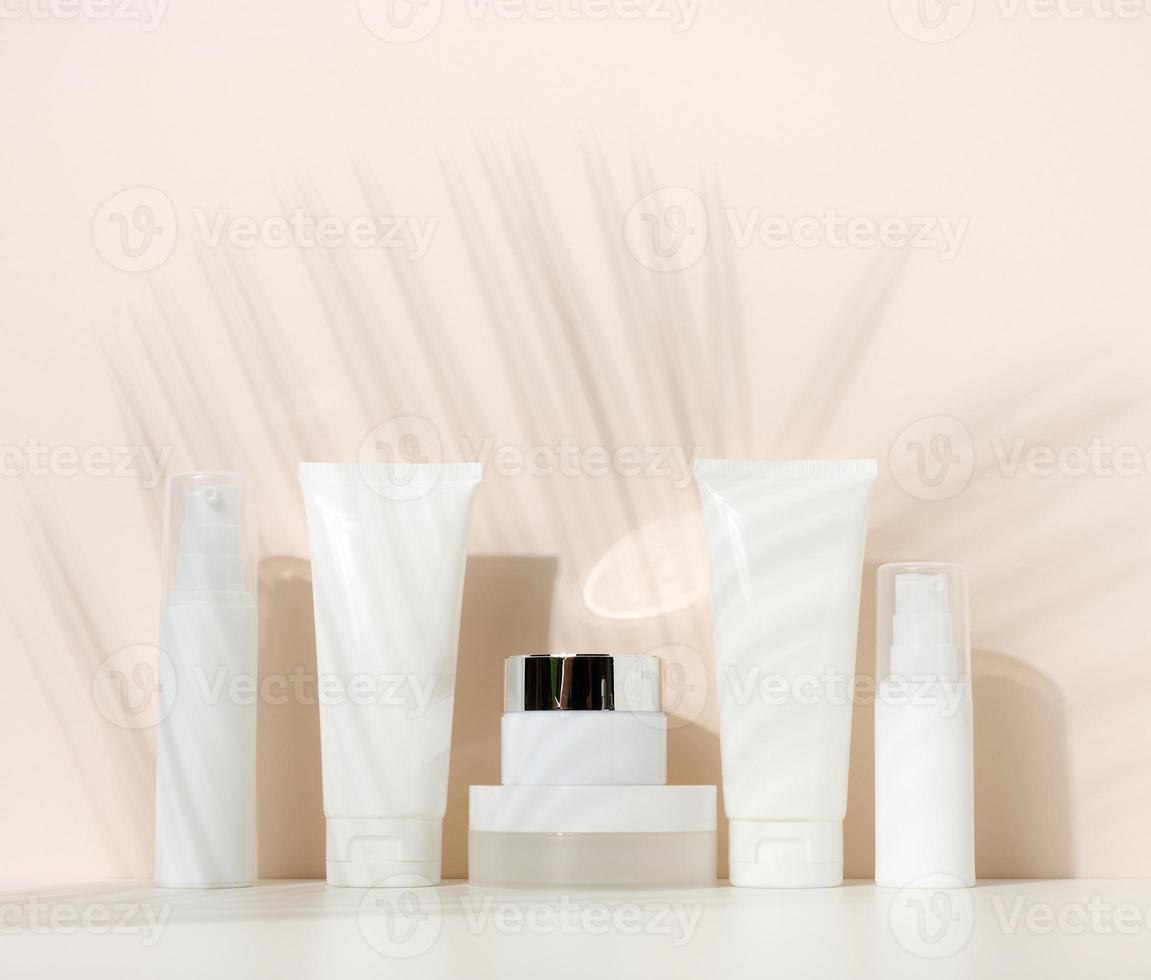 pot, bouteille et tubes en plastique blanc vides pour cosmétiques sur fond beige. emballage pour crème, gel, sérum, publicité et promotion de produits photo