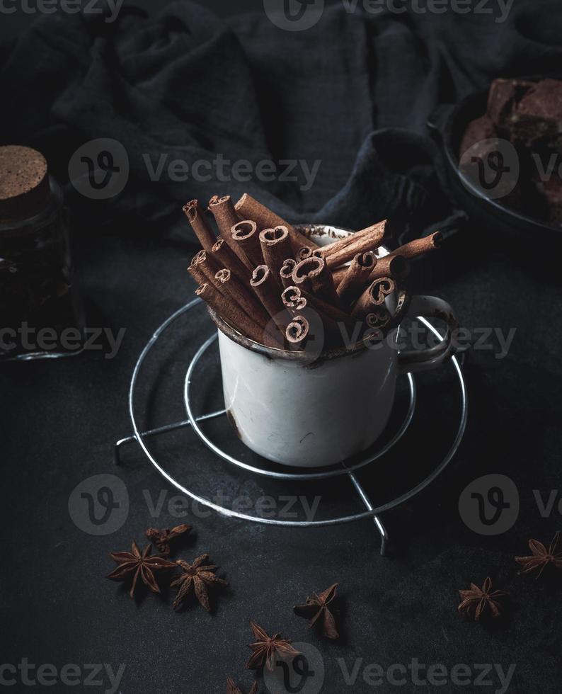 bâtons de cannelle dans une vieille tasse en métal sur un tableau noir. épice aromatique photo