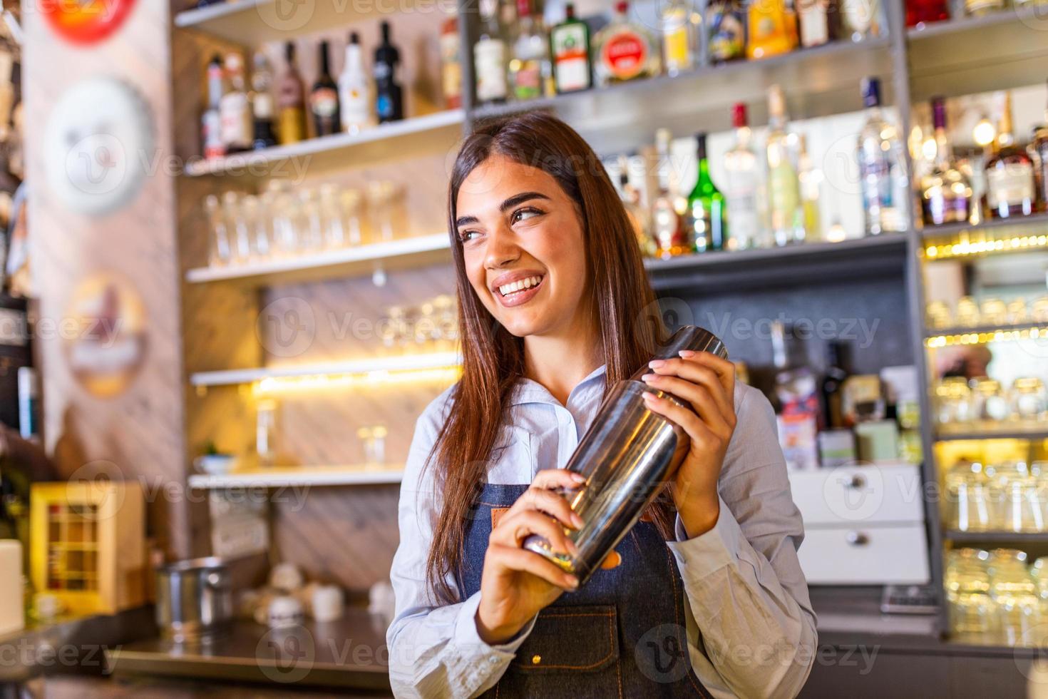 jeune travailleuse au bureau du barman dans le bar du restaurant préparant un cocktail avec un shaker. belle jeune femme derrière un bar faisant un cocktail photo